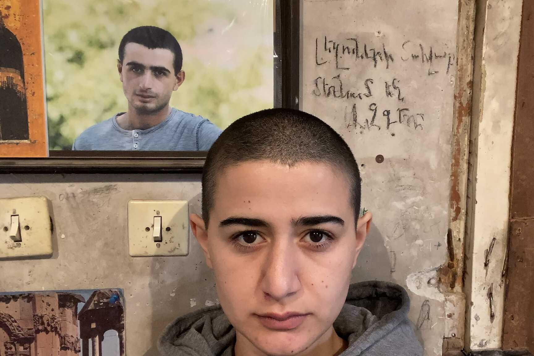 Shoghakat Vardanyan standing in front of a picture of her brother, Soghomon Vardanyan. Film still.